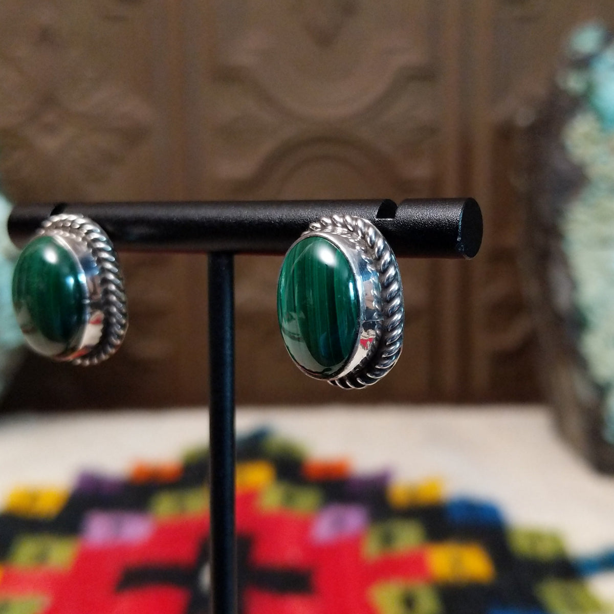 Malachite Oval Earrings by Priscilla Smith featuring polished deep-green malachite cabochons with natural banding, set in silver with twisted rope-style borders; side view.