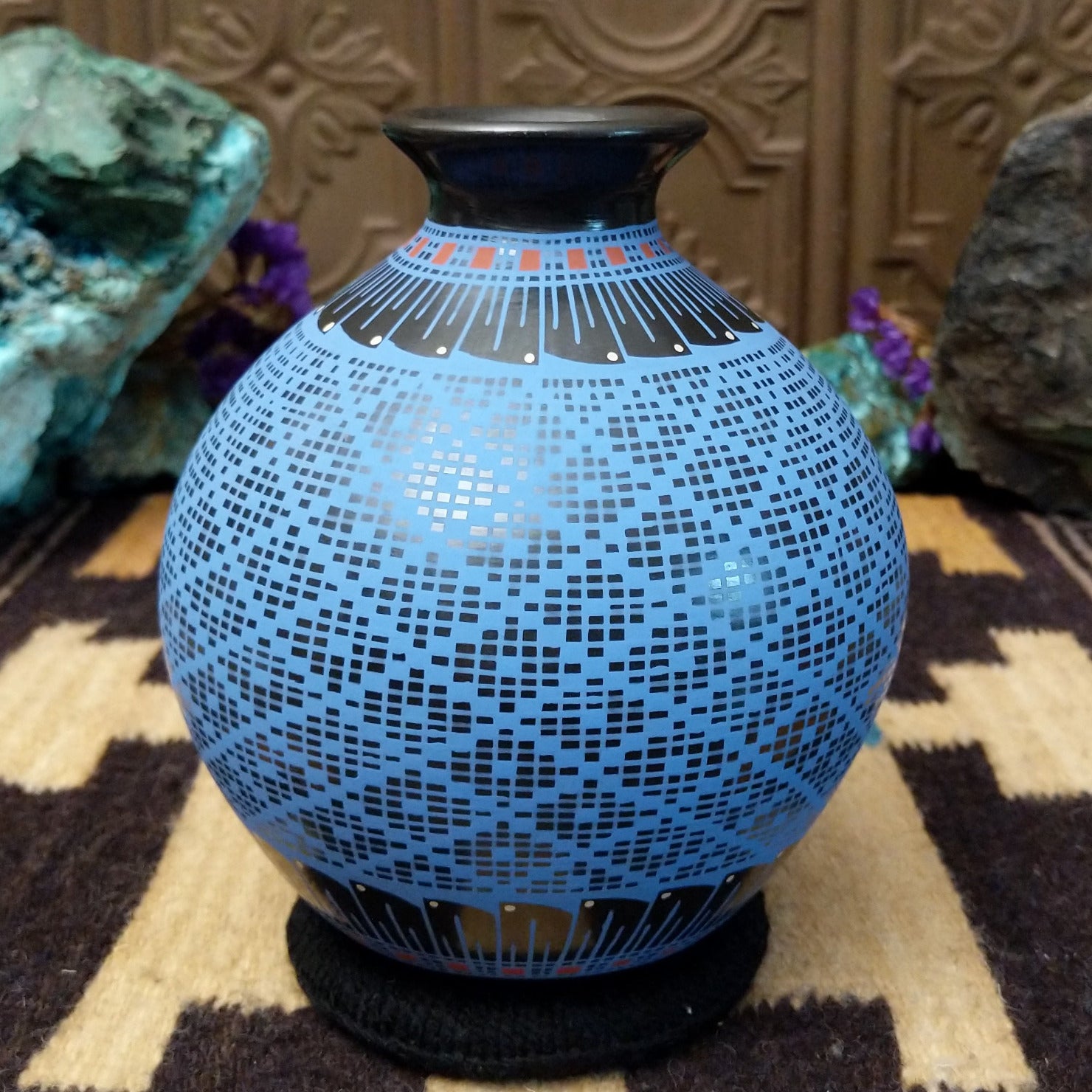 Blue Mata Ortiz pottery vase with a flared black neck, featuring intricate geometric patterns of small black squares and red accent details near the rim.