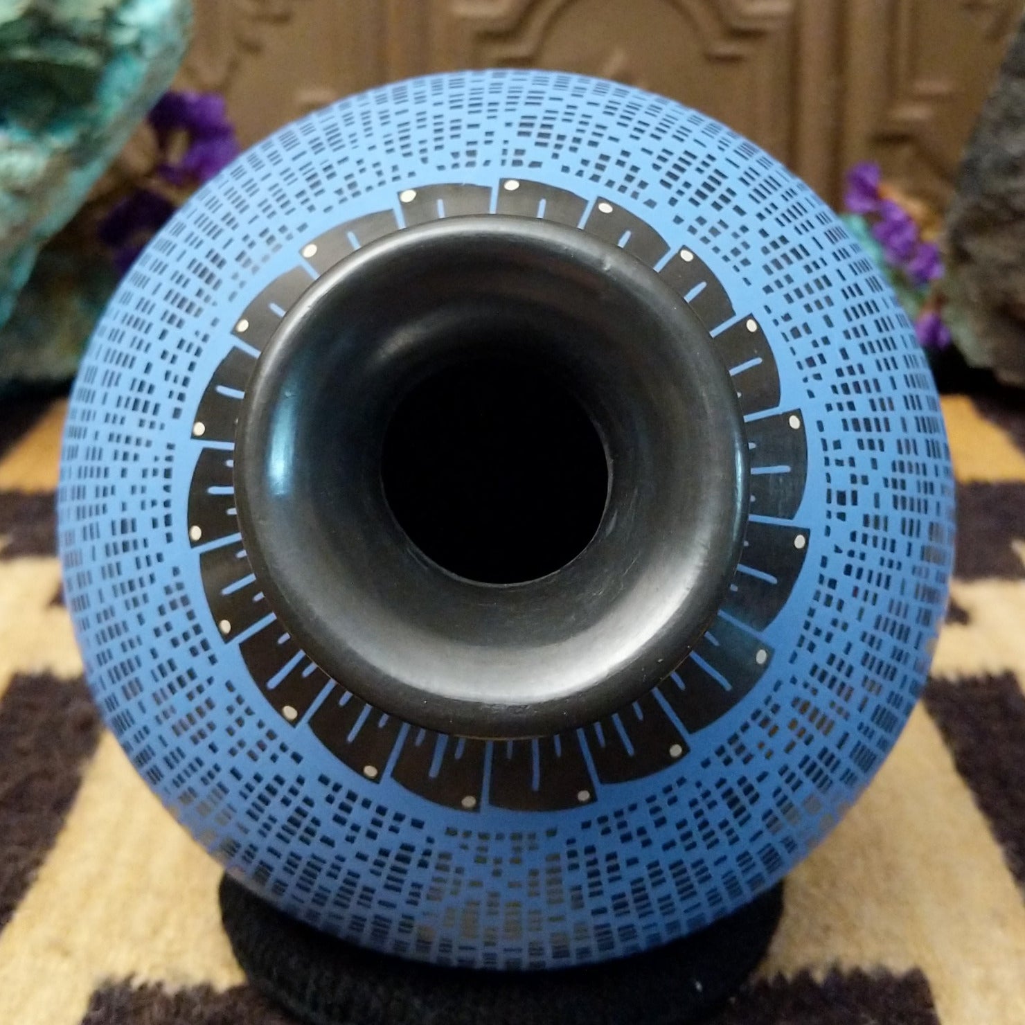 Blue Mata Ortiz pottery vase with a flared black neck, featuring intricate geometric patterns of small black squares and red accent details near the rim.
