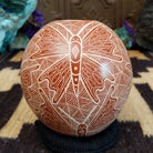 Round Mata Ortiz pottery vessel featuring an etched butterfly design in warm clay tones with intricate geometric linework across the surface.