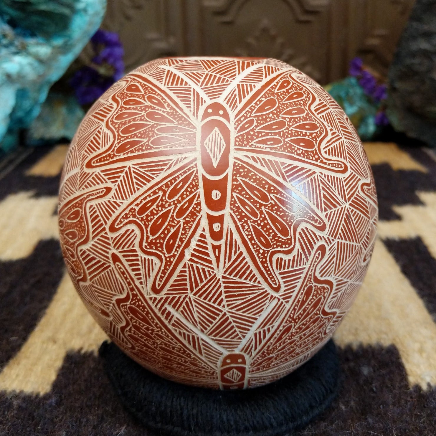 Round Mata Ortiz pottery vessel featuring an etched butterfly design in warm clay tones with intricate geometric linework across the surface.