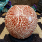 Round Mata Ortiz pottery vessel featuring an etched butterfly design in warm clay tones with intricate geometric linework across the surface.