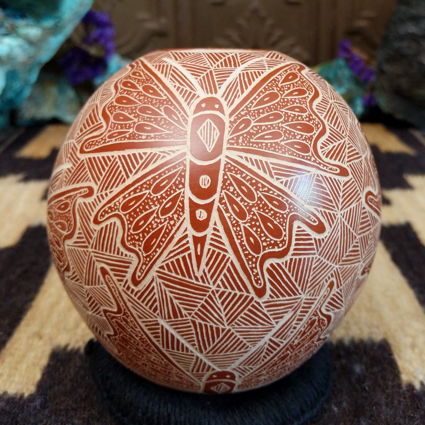 Round Mata Ortiz pottery vessel featuring an etched butterfly design in warm clay tones with intricate geometric linework across the surface.