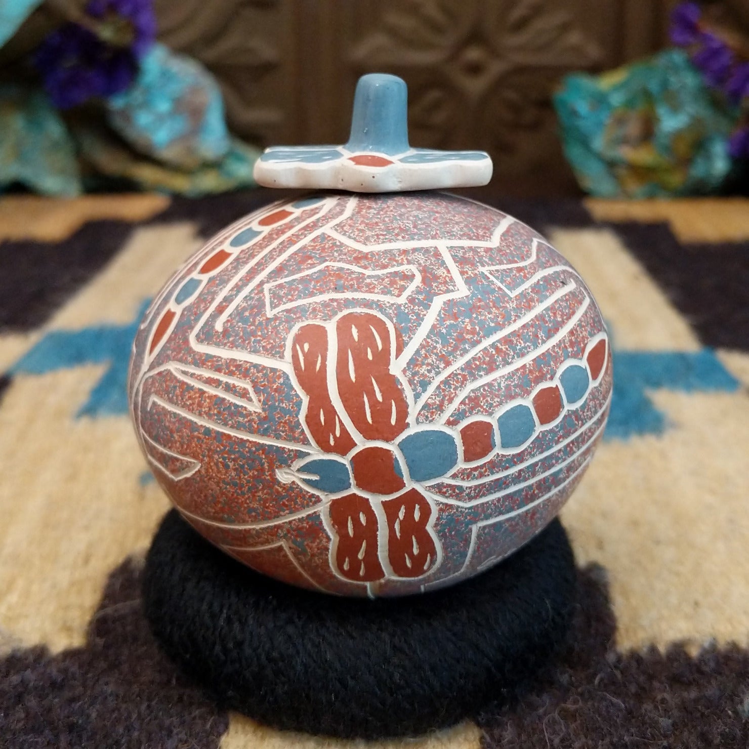 Round lidded Mata Ortiz pottery vessel featuring a dragonfly design in blue and clay tones with etched geometric background patterns.