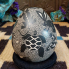 Egg-shaped Mata Ortiz pottery vessel with an etched black and white wildlife design featuring multiple stylized animals.