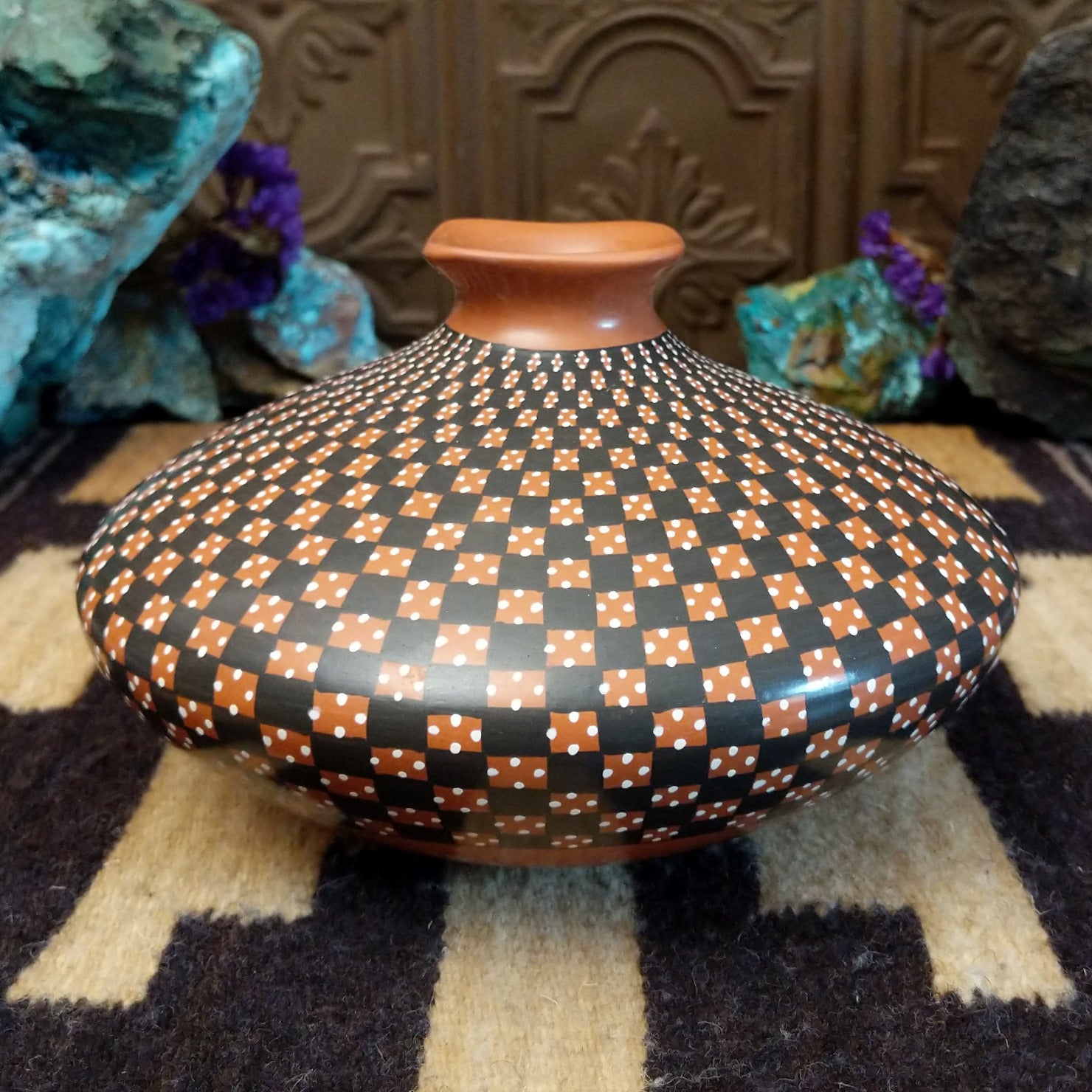 Low-profile Mata Ortiz pottery jar with a geometric checkerboard pattern in black and clay tones, featuring white dotted accents and a squared neck opening.