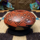 Rounded Mata Ortiz seed pot with a red clay finish, featuring a radiating geometric mosaic pattern of black and white squares and a black decorative band near the base.