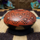 Rounded Mata Ortiz seed pot with a red clay finish, featuring a radiating geometric mosaic pattern of black and white squares and a black decorative band near the base.