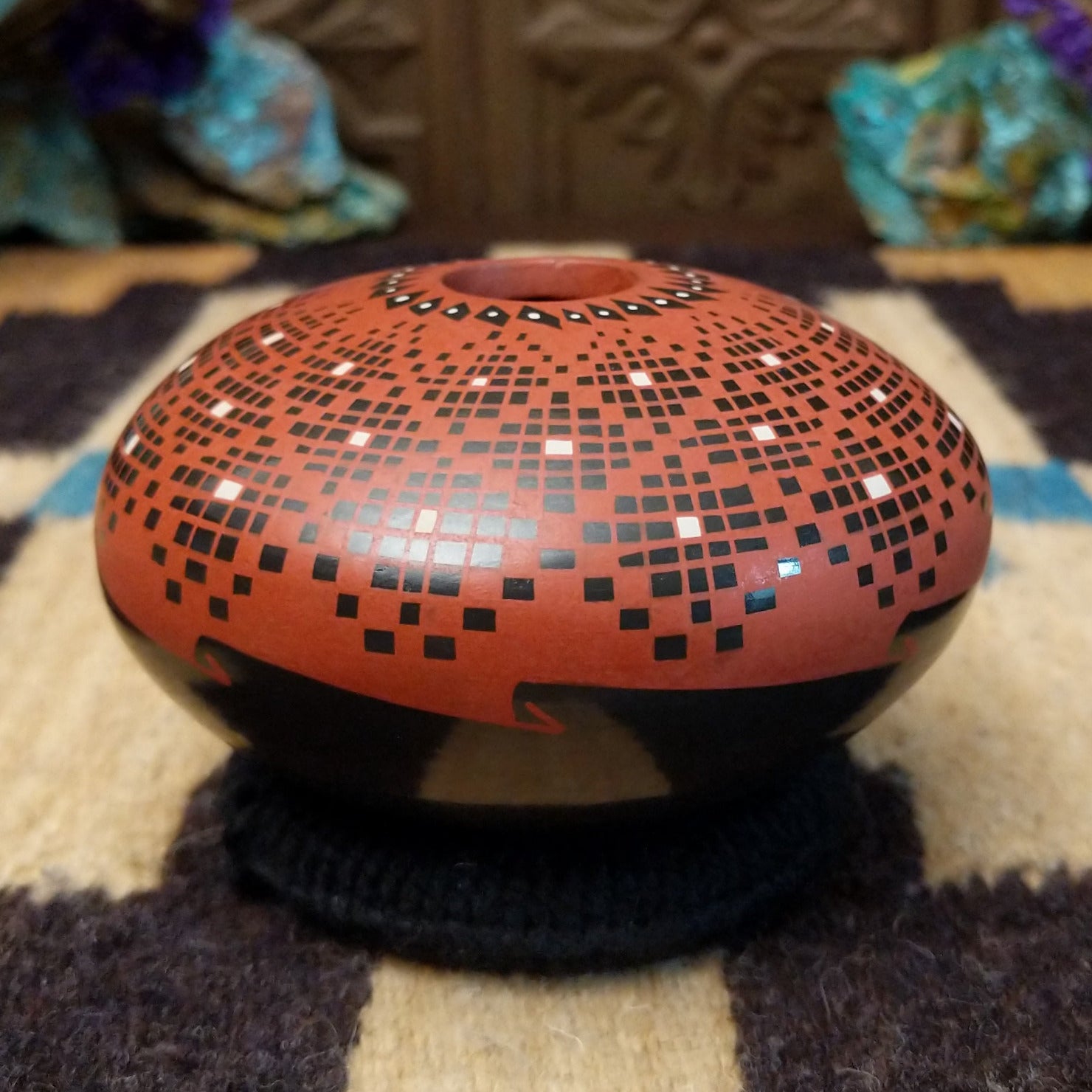 Rounded Mata Ortiz seed pot with a red clay finish, featuring a radiating geometric mosaic pattern of black and white squares and a black decorative band near the base.