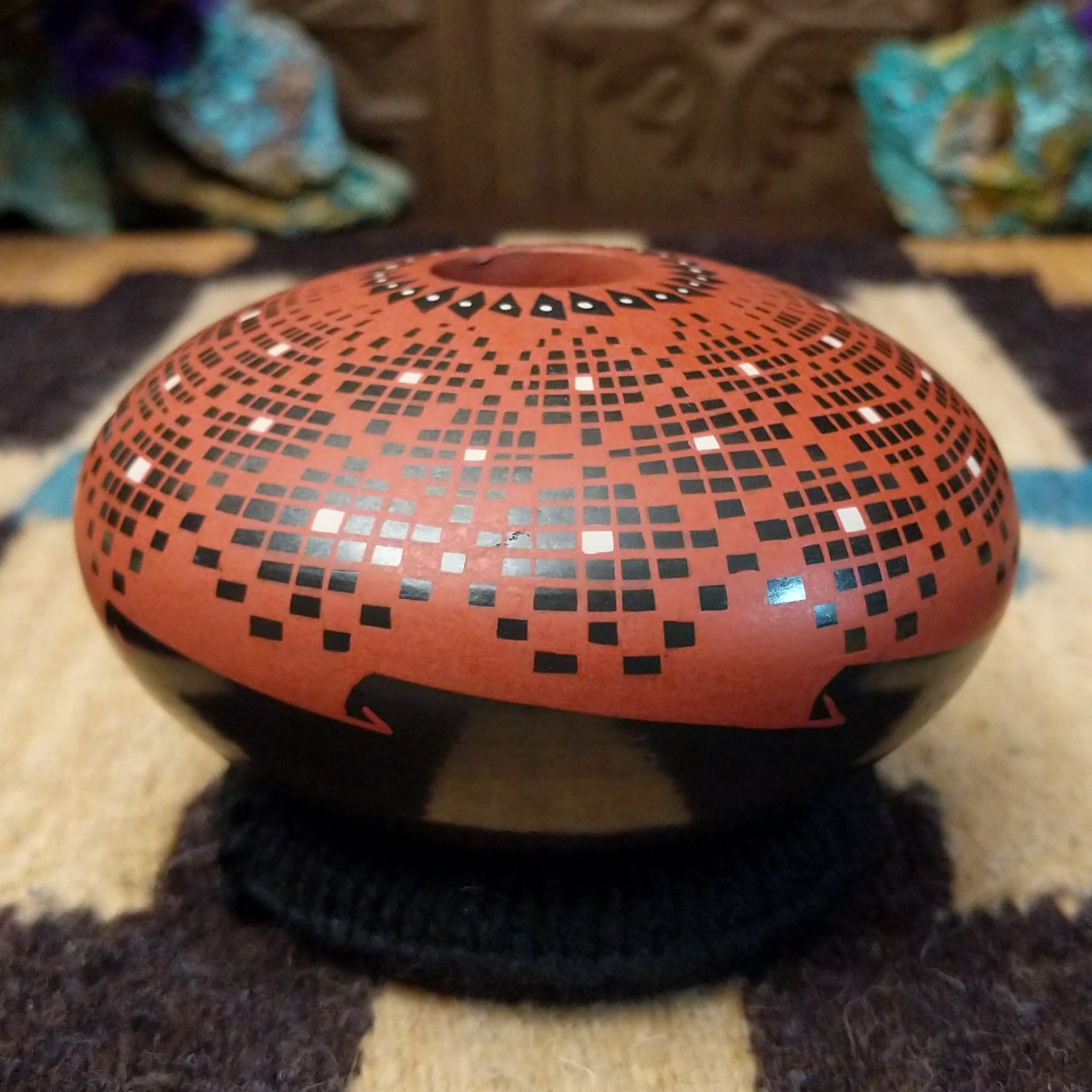 Rounded Mata Ortiz seed pot with a red clay finish, featuring a radiating geometric mosaic pattern of black and white squares and a black decorative band near the base.