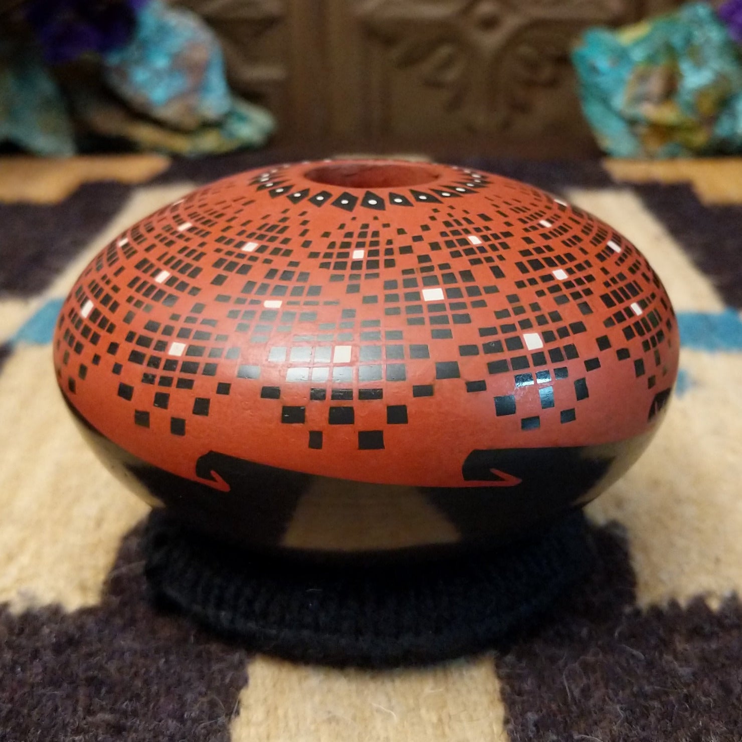 Rounded Mata Ortiz seed pot with a red clay finish, featuring a radiating geometric mosaic pattern of black and white squares and a black decorative band near the base.