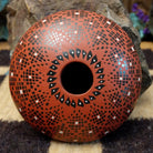 Rounded Mata Ortiz seed pot with a red clay finish, featuring a radiating geometric mosaic pattern of black and white squares and a black decorative band near the base.