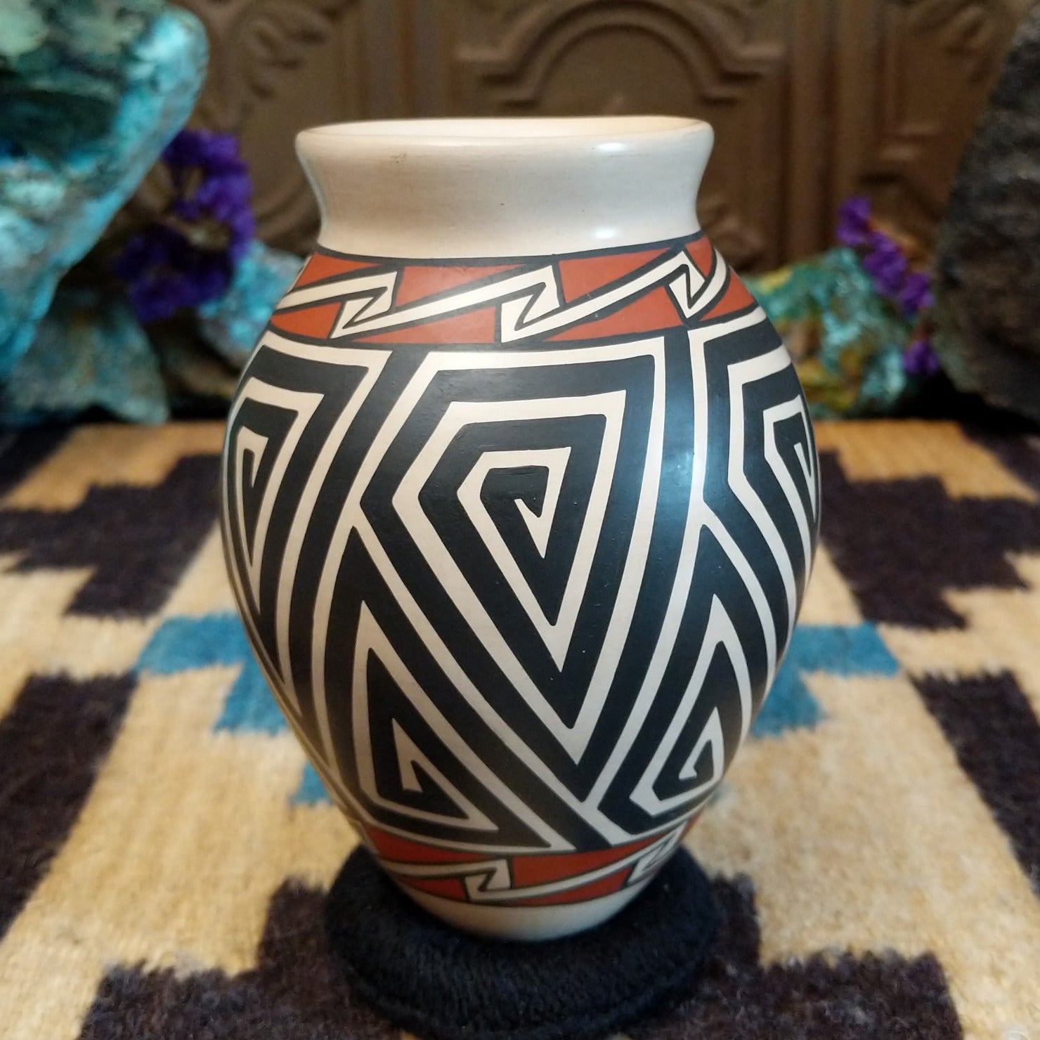 Mata Ortiz pottery vase with a cream rim, featuring bold black and cream triangle spiral patterns with warm clay accents near the neck.
