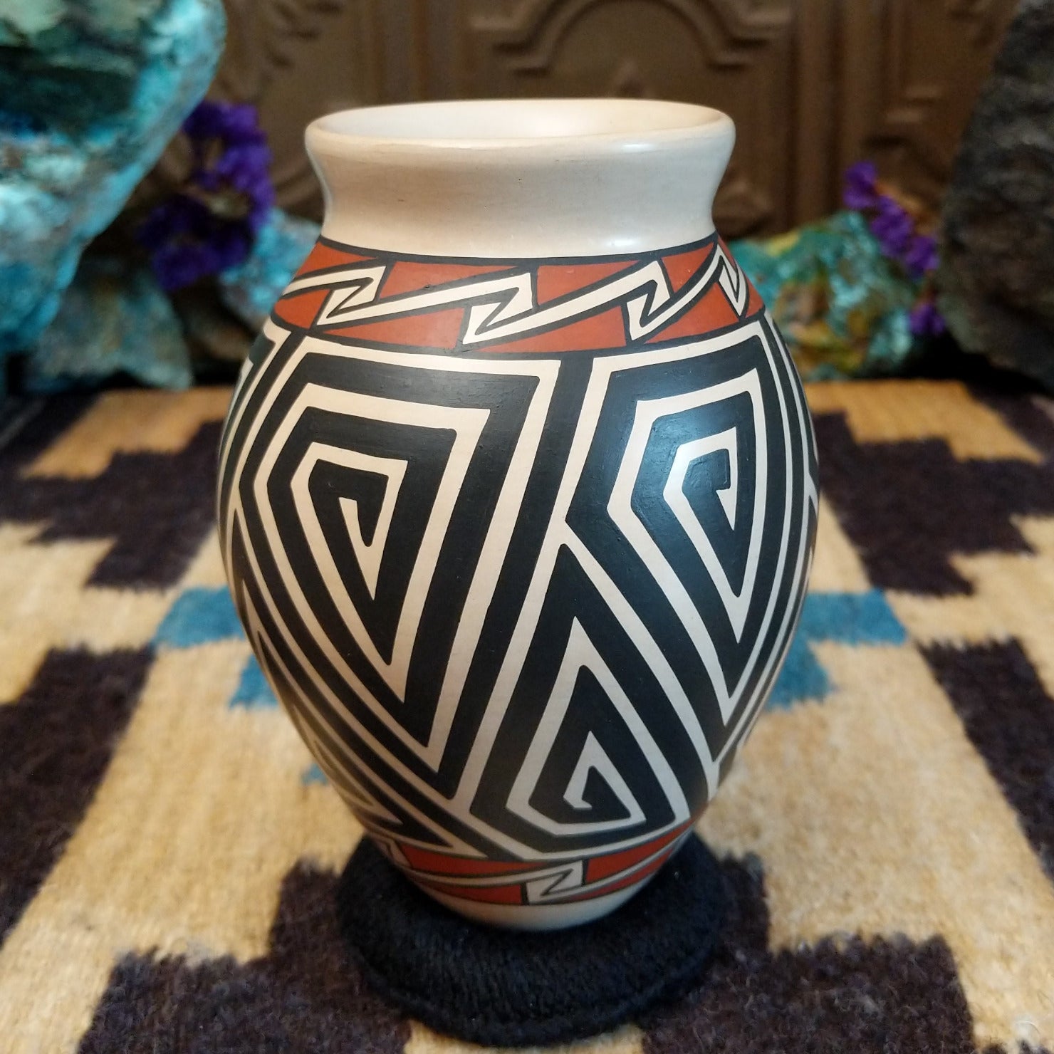 Mata Ortiz pottery vase with a cream rim, featuring bold black and cream triangle spiral patterns with warm clay accents near the neck.