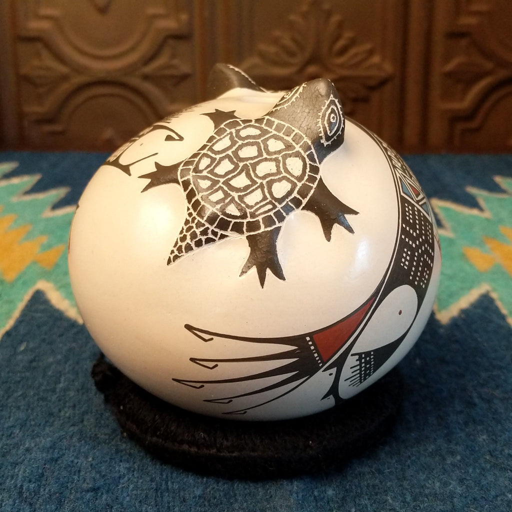 White clay with turtle motifs and geometric designs painted traditional colors on the seed pot.