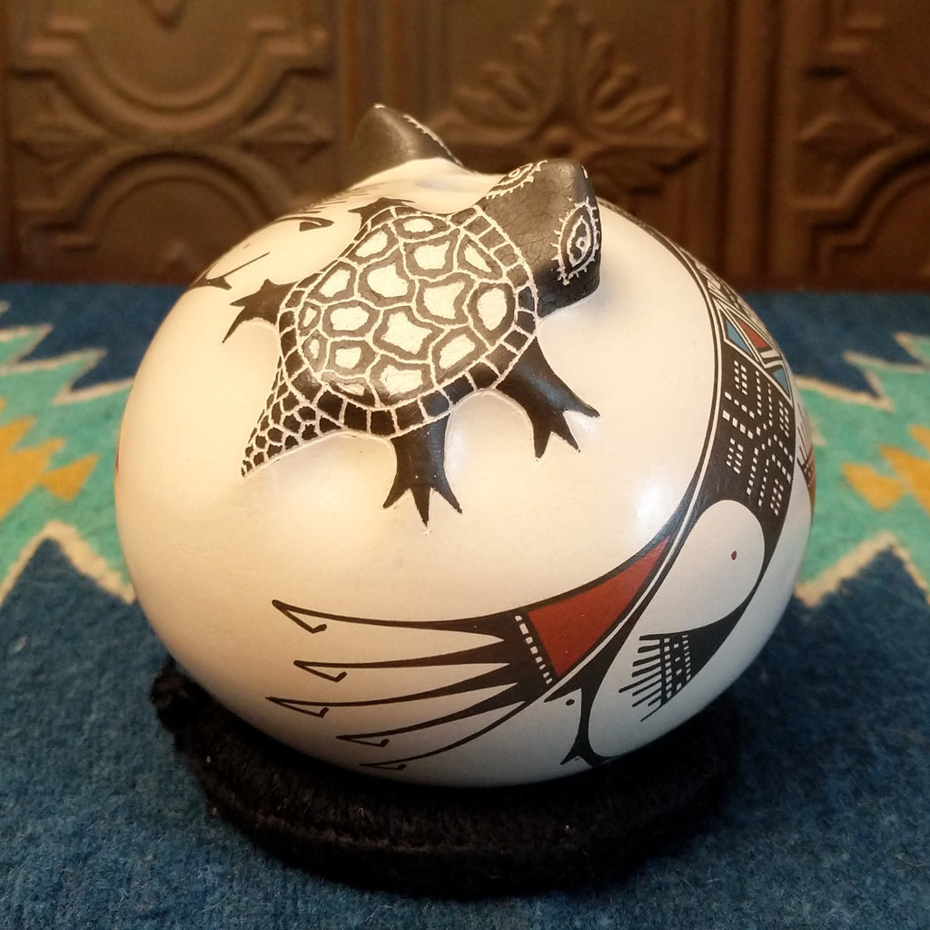 White clay with turtle motifs and geometric designs painted traditional colors on the seed pot.