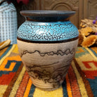 Mini horsehair pottery vase by Roger Calhoun with a flared dark rim, crackled turquoise-blue shoulder, and black horsehair markings concentrated near the base of its cream-colored body.