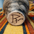 Close-up of the underside of Roger Calhoun's horsehair pottery, showing the artist's hand-painted initials on the unglazed base.