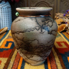 This charming Mini Mottled Green Horsehair Pottery by Roger Calhoun features a rounded vase with a flared black rim, earthy tones, soft green accents, intricate black horsehair patterns, and a copper wire with a green bead.