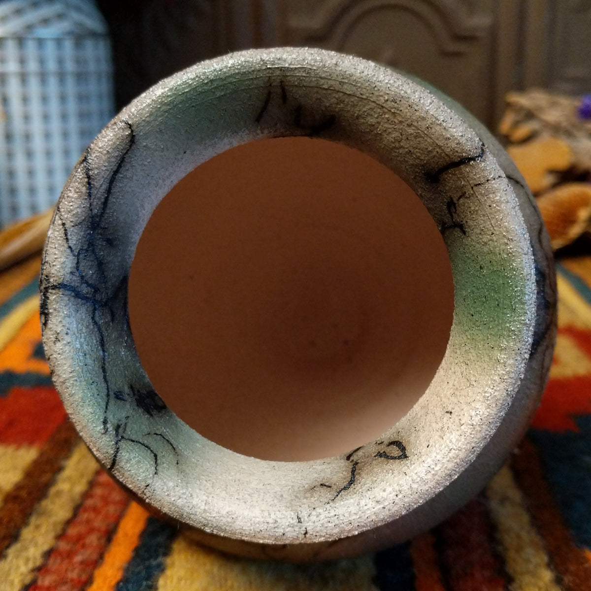 This charming Mini Mottled Green Horsehair Pottery by Roger Calhoun features a rounded vase with a flared black rim, earthy tones, soft green accents, intricate black horsehair patterns, and a copper wire with a green bead; top view.