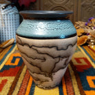 Mini horsehair pottery vase by Roger Calhoun with a flared dark rim, crackled turquoise-blue shoulder, and black horsehair markings concentrated near the base of its cream-colored body.