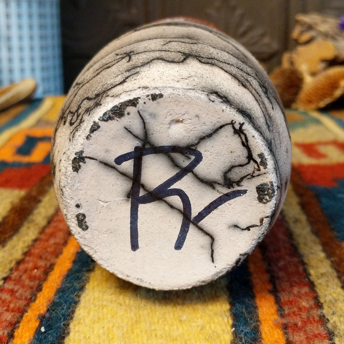 Close-up of the underside of Roger Calhoun's horsehair pottery, showing the artist's hand-painted initials on the unglazed base.