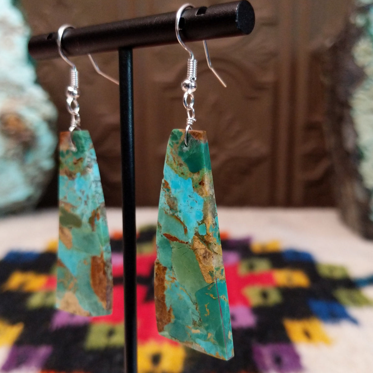 Mohave Turquoise Slab Earrings by Jameson Pete featuring elongated geometric turquoise stones with blue, green, tan, and brown matrix, suspended from silver hooks; side view.