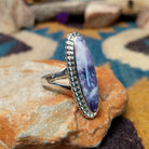 Handcrafted sterling silver ring featuring an elongated marquise-shaped Morado Opal cabochon with swirling shades of lavender, deep purple, and creamy white, set in a polished sterling silver beaded bezel; side view.