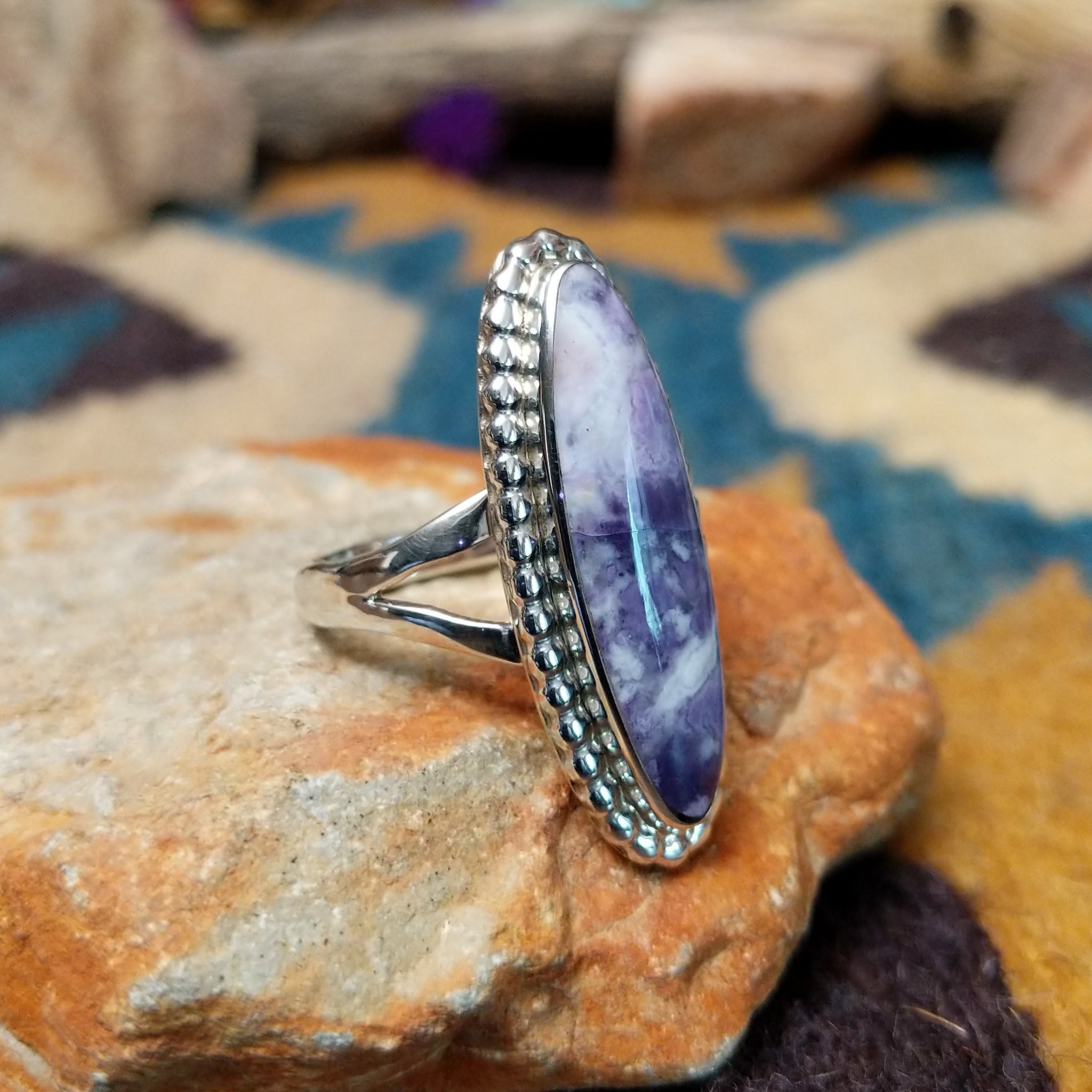 Handcrafted sterling silver ring featuring an elongated marquise-shaped Morado Opal cabochon with swirling shades of lavender, deep purple, and creamy white, set in a polished sterling silver beaded bezel; side view.