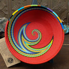 Handwoven multicolor wire art bowl by Bridge for Africa featuring a vibrant spiral design made from recycled wire in bold red, blue, green, yellow, orange, purple, and black tones.