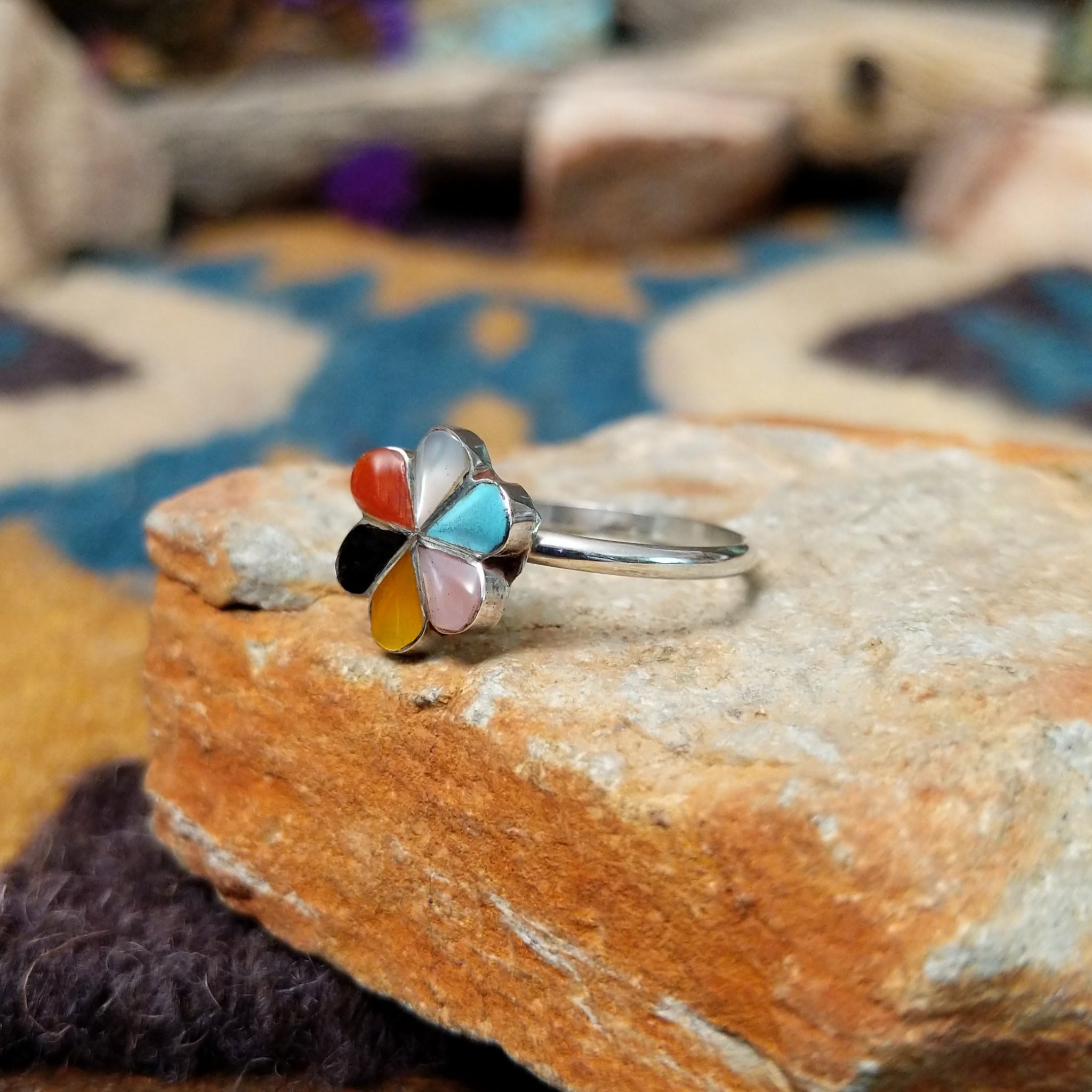 Handcrafted Zuni sterling silver flower ring by Raymond Bobelu featuring a six-petal multistone inlay design with turquoise, coral, black onyx, mother of pearl, and yellow mussel shell; side view.