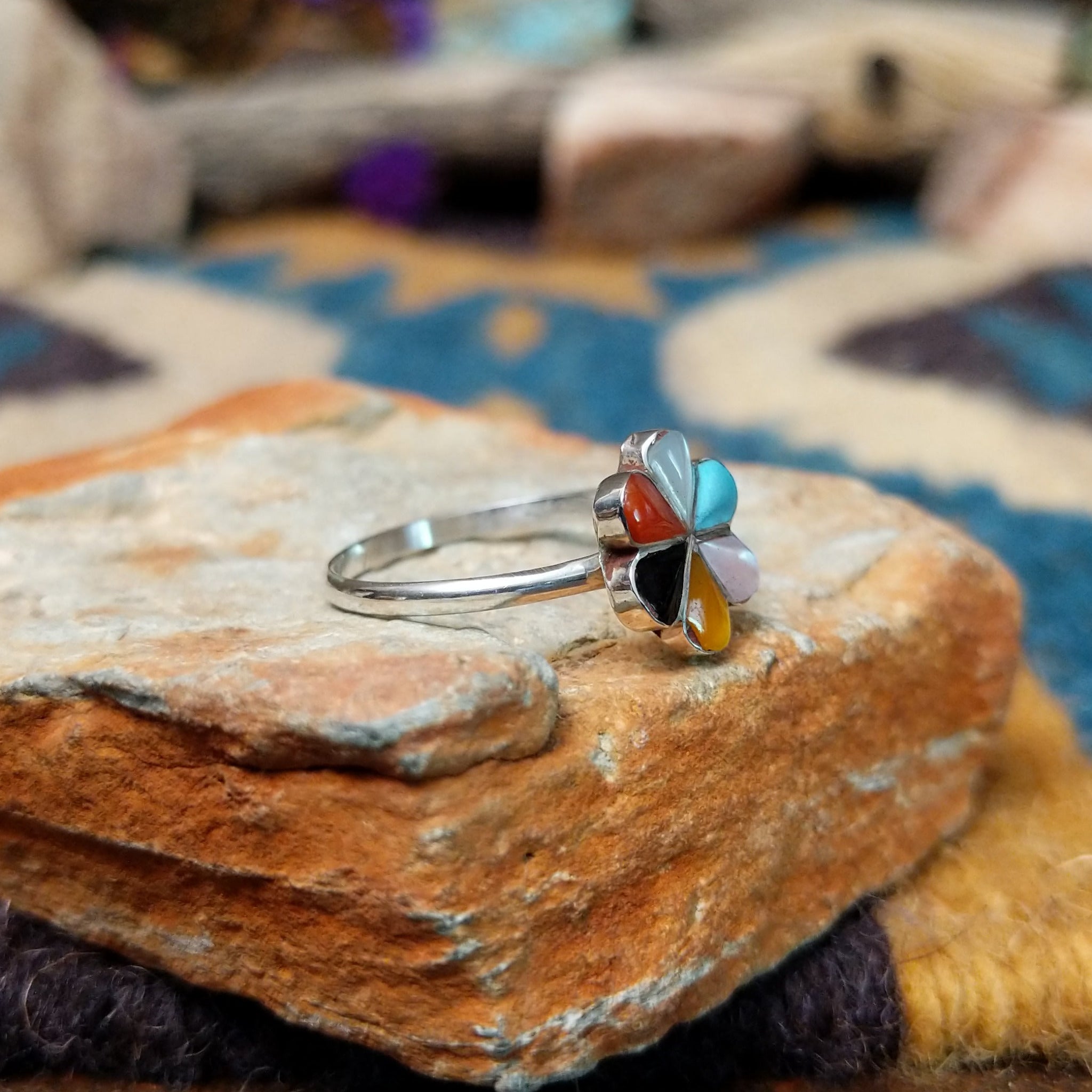 Handcrafted Zuni sterling silver flower ring by Raymond Bobelu featuring a six-petal multistone inlay design with turquoise, coral, black onyx, mother of pearl, and yellow mussel shell; side view.