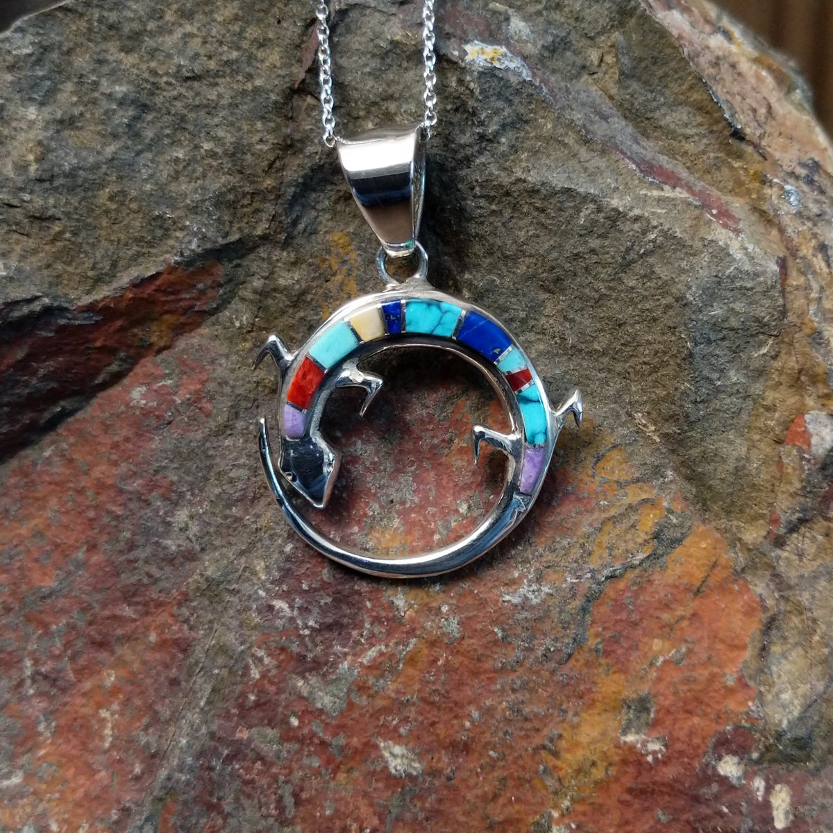 Multistone inlay lizard pendant by Ambrose Tsosie featuring a circular sterling silver lizard design accented with turquoise, blue, red, purple, and cream-colored stone inlay.