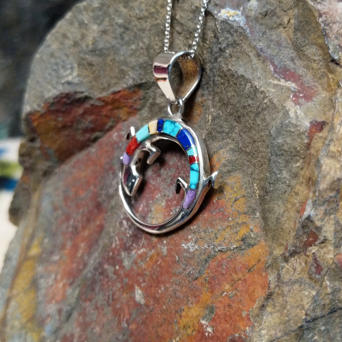 Multistone inlay lizard pendant by Ambrose Tsosie featuring a circular sterling silver lizard design accented with turquoise, blue, red, purple, and cream-colored stone inlay; side view.