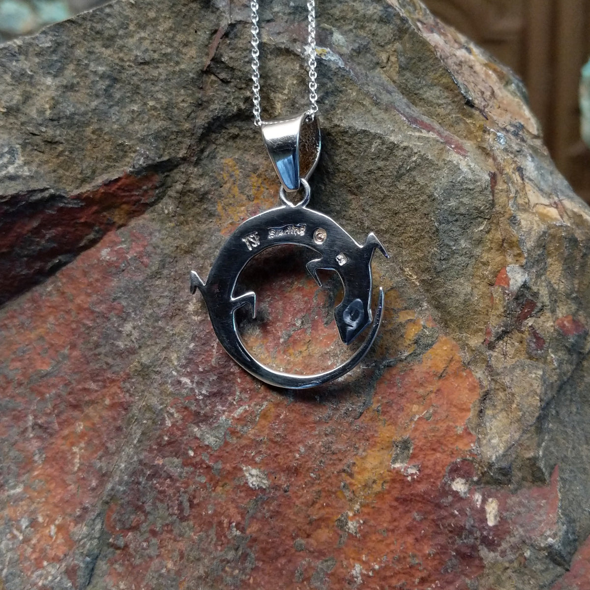 Multistone inlay lizard pendant by Ambrose Tsosie featuring a circular sterling silver lizard design accented with turquoise, blue, red, purple, and cream-colored stone inlay; artisan and Sterling Silver stamp.