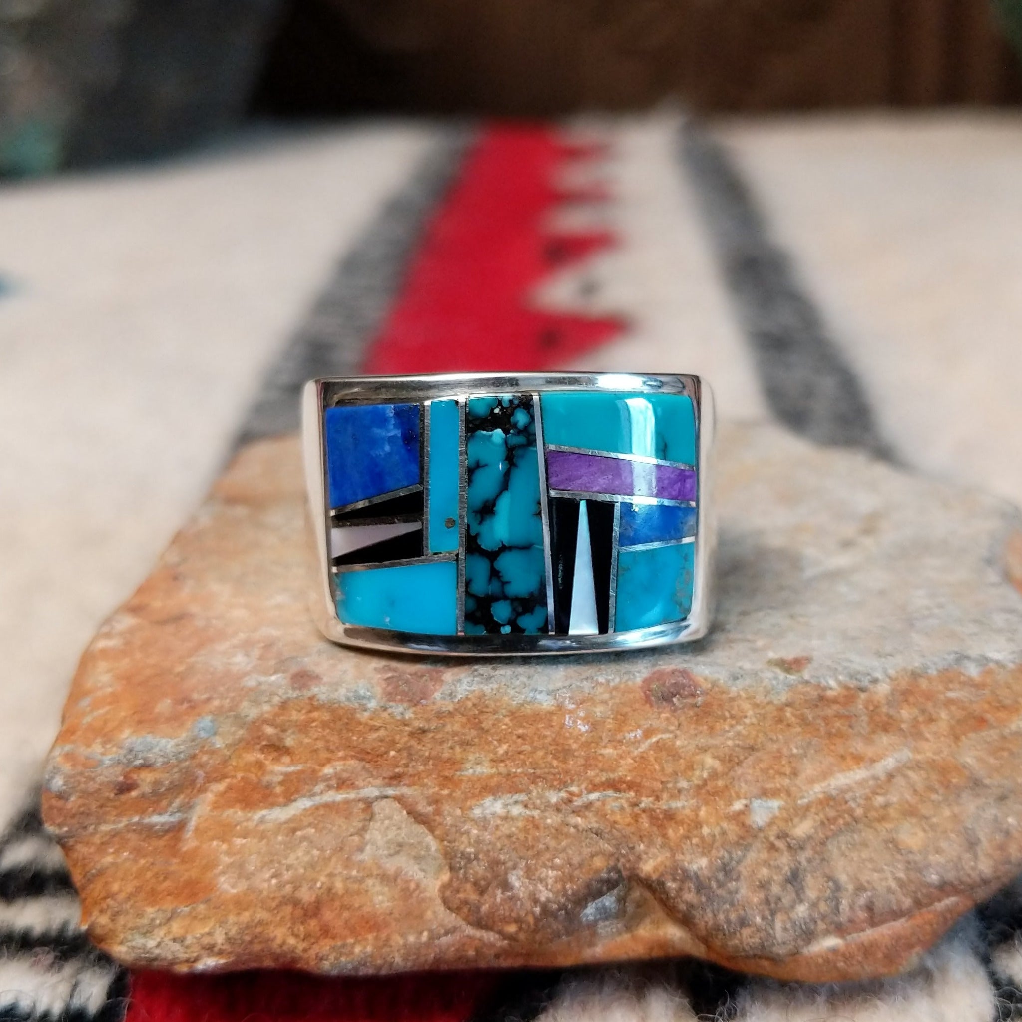 Multistone inlay ring by E.D. featuring geometric turquoise, blue, purple, black, and light-colored stones separated by fine silver channels in a wide polished silver setting.