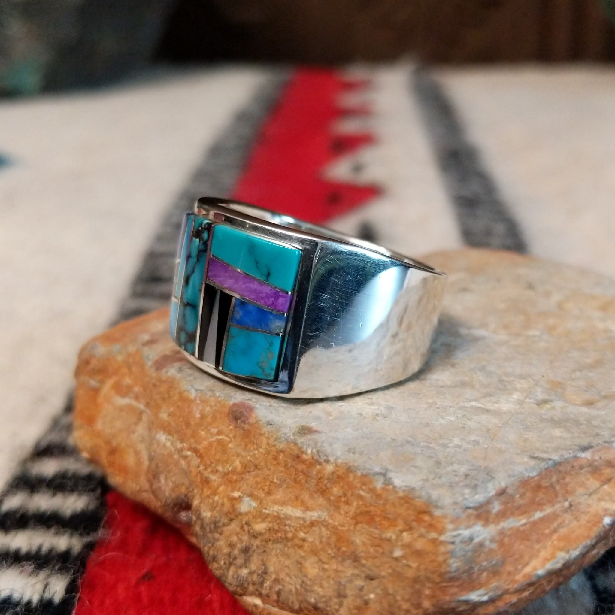 Multistone inlay ring by E.D. featuring geometric turquoise, blue, purple, black, and light-colored stones separated by fine silver channels in a wide polished silver setting; side view.