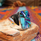Multistone Inlay Ring by E.D. featuring a large rectangular face with geometric turquoise, blue, purple, cream, and multicolored stone inlay separated by fine silver channels; side view.