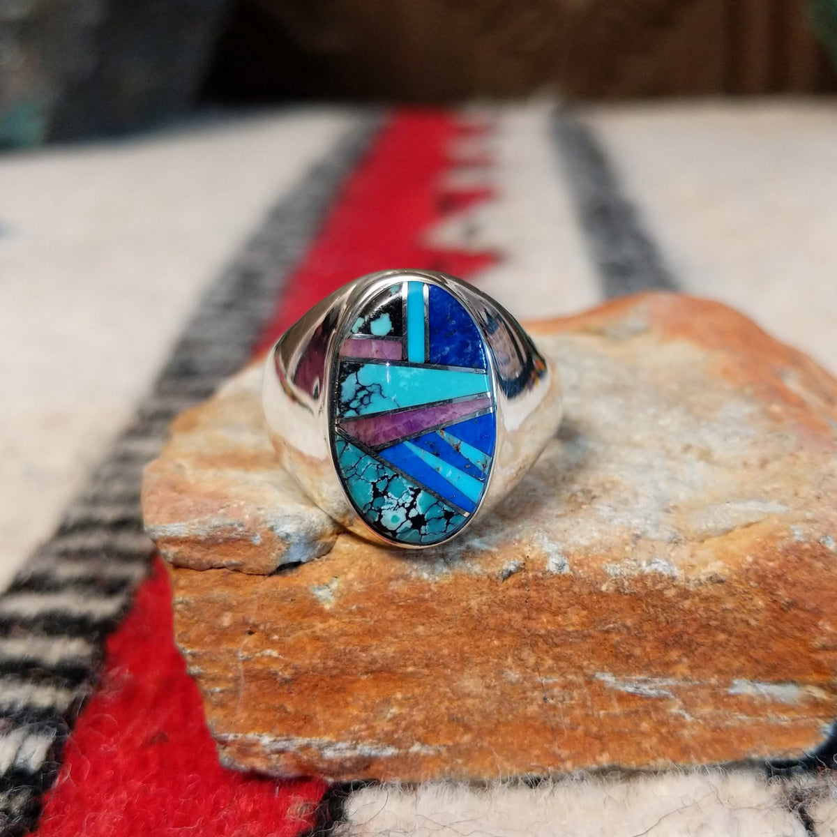 Multistone inlay ring by P.D. featuring an oval geometric design with turquoise, blue, purple, and black stones set in a polished silver band.