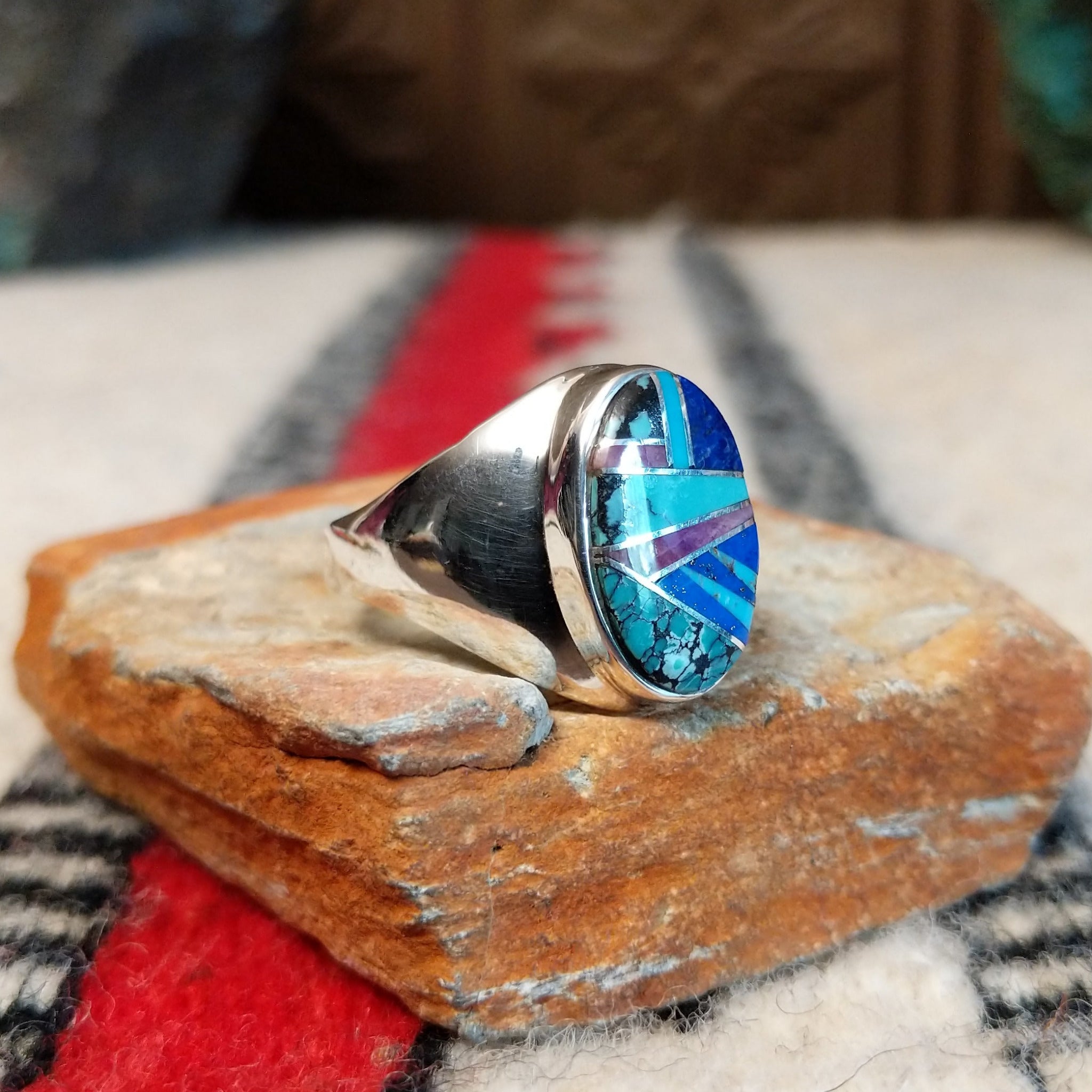 Multistone inlay ring by P.D. featuring an oval geometric design with turquoise, blue, purple, and black stones set in a polished silver band; side view.