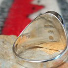 Multistone inlay ring by P.D. featuring an oval geometric design with turquoise, blue, purple, and black stones set in a polished silver band; artisan and Sterling Silver stamp.
