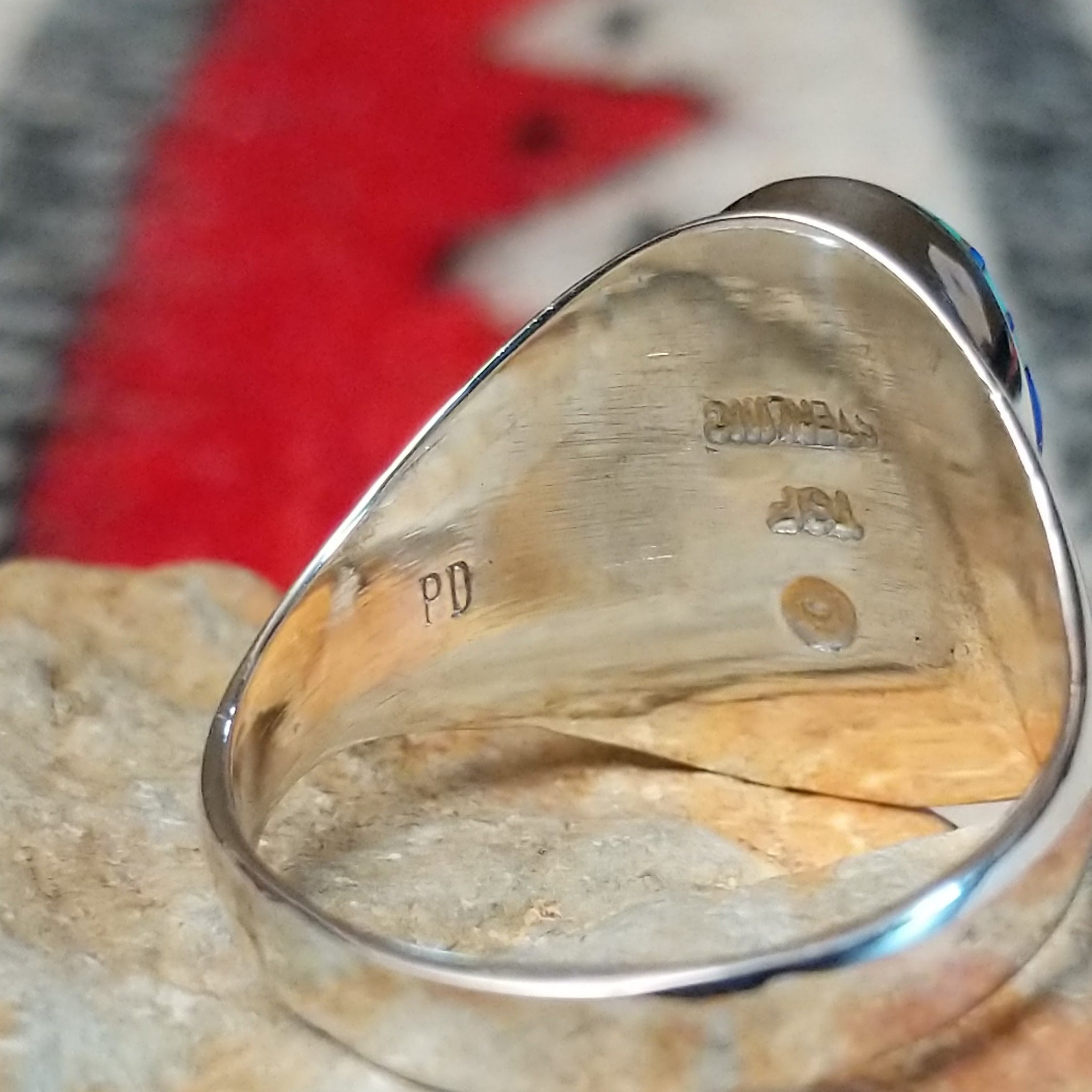 Multistone inlay ring by P.D. featuring an oval geometric design with turquoise, blue, purple, and black stones set in a polished silver band; artisan and Sterling Silver stamp.