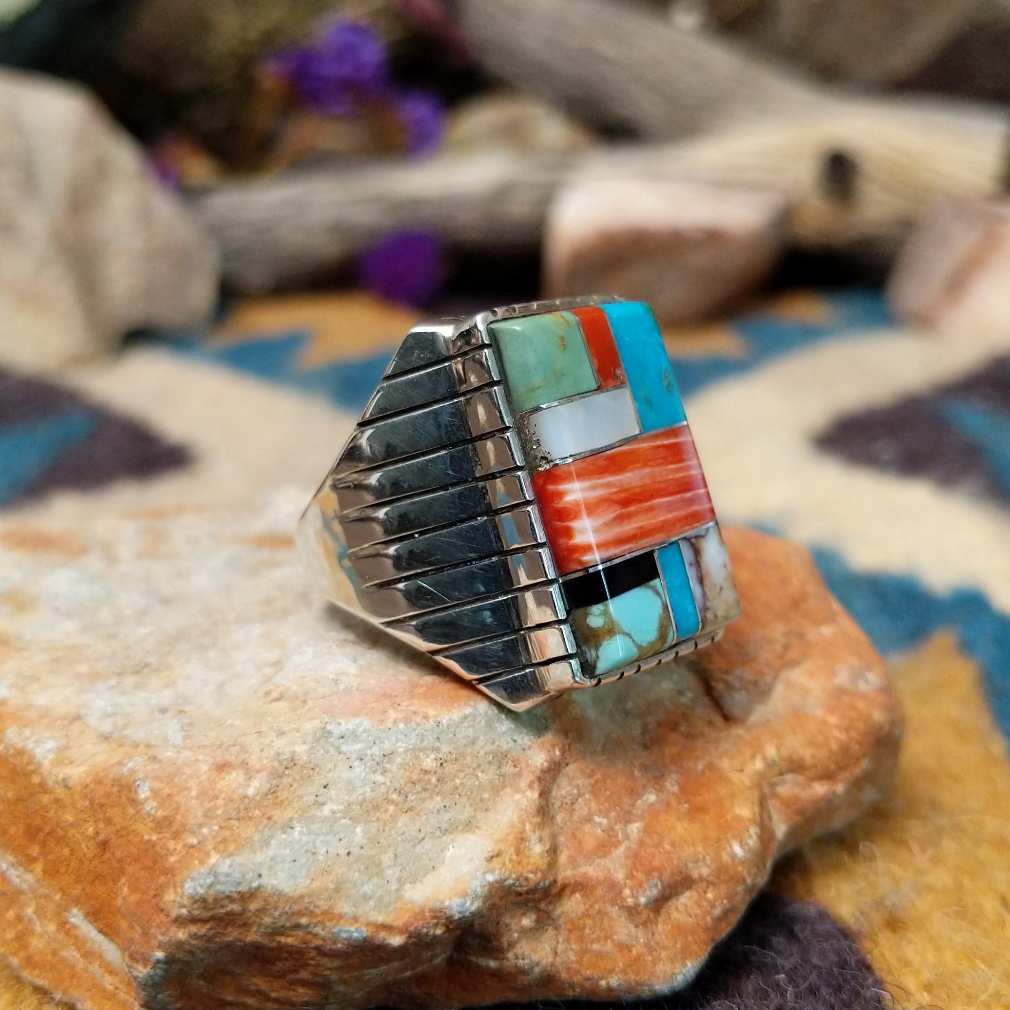 Sterling silver multistone inlay ring by Rex Abeita featuring turquoise, red coral, mother-of-pearl, black onyx, and a geometric mosaic design; side view.
