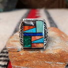 Multistone inlay ring by Terry Wood featuring a rectangular geometric design with turquoise, blue, green, orange, peach, and black stones set in silver with detailed scrollwork along the sides.