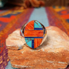 Multistone Inlay Ring by Wilbert Grey featuring an oval geometric design of orange, turquoise, and deep blue stones separated by fine silver channels in a polished silver setting.