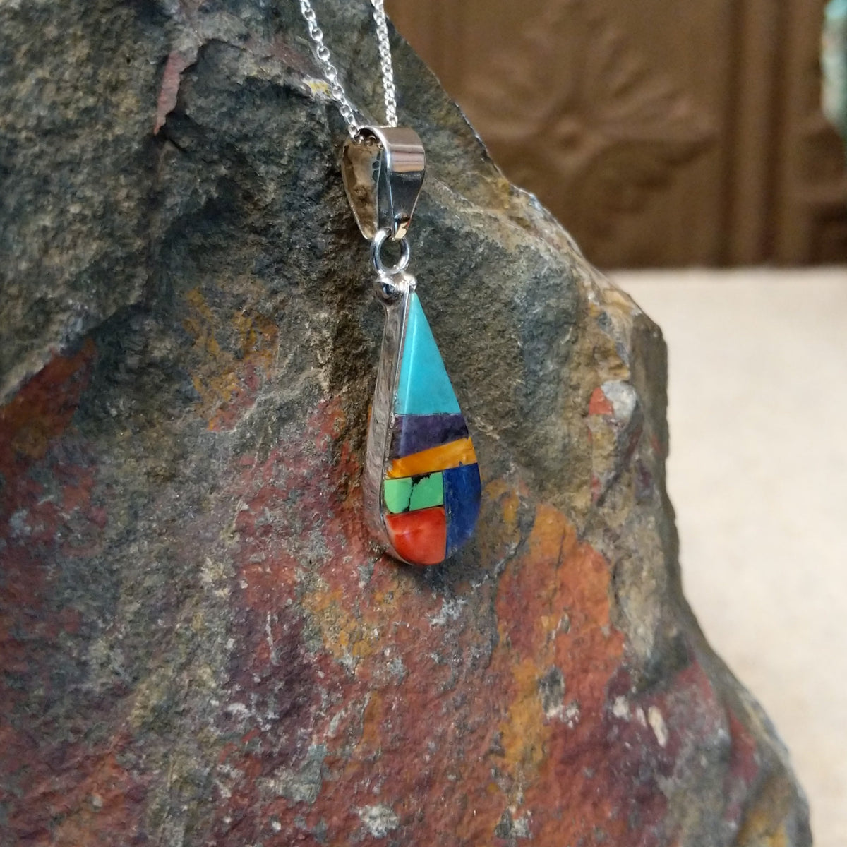 Multistone inlay teardrop pendant by P. Smith featuring turquoise, purple, orange, green, red, and blue stones arranged in a colorful geometric design; side view.