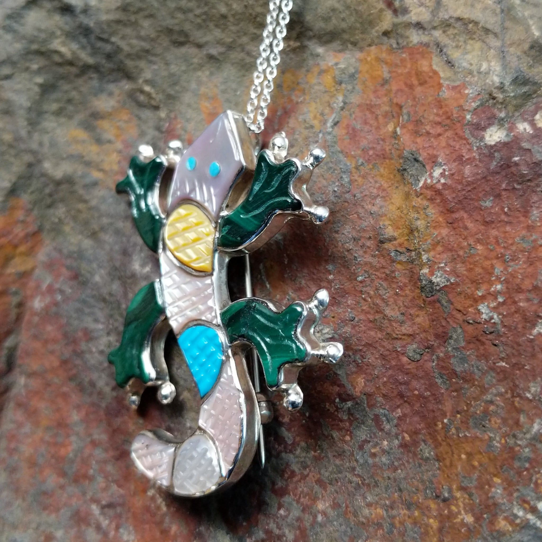 Handcrafted sterling silver multistone lizard pin and pendant by Tamara Pinto, featuring traditional Zuni inlay in a colorful lizard design; side view.