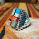 This vibrant Multistone Rectangle Inlay Ring by Wilbert Grey features a geometric arrangement of turquoise, coral, black, and white stone inlays set in a rectangular silver face with a detailed band; side view.