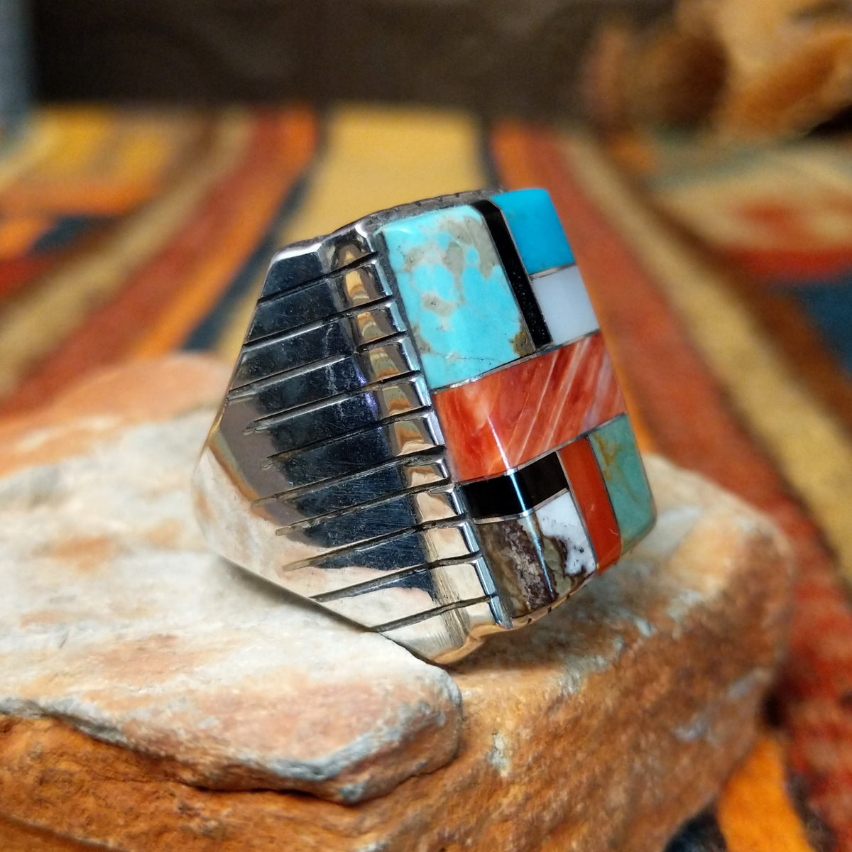 This vibrant Multistone Rectangle Inlay Ring by Wilbert Grey features a geometric arrangement of turquoise, coral, black, and white stone inlays set in a rectangular silver face with a detailed band; side view.