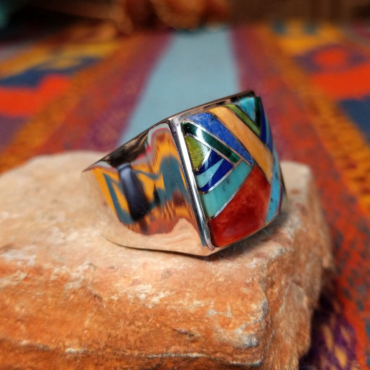 Multistone Square Inlay Ring by O.J. featuring colorful geometric turquoise, blue, red, yellow, and green stone inlay separated by Sterling Silver channels on a broad square face; side view.